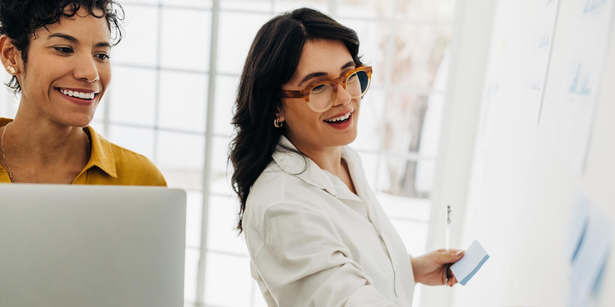 Two business women sticking their business ideas to a wall in an office.